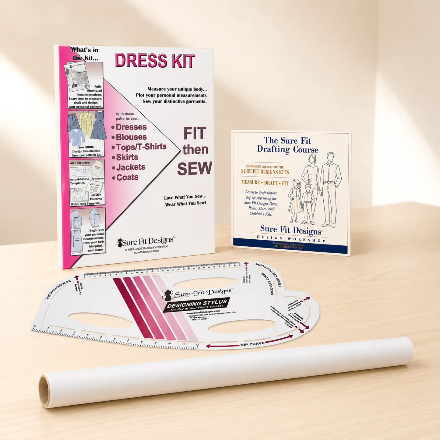 A sewing dress kit set displayed on a light wood surface, including a printed instruction booklet, a drafting course card, a curved measuring ruler, and a roll of white fabric.