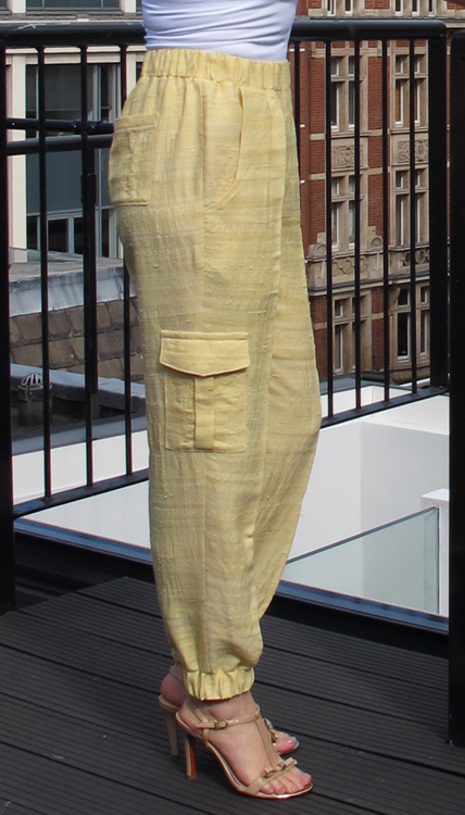 A pair of woven yellow joggers with a high waist and cargo pockets, modeled against an outdoor backdrop.
