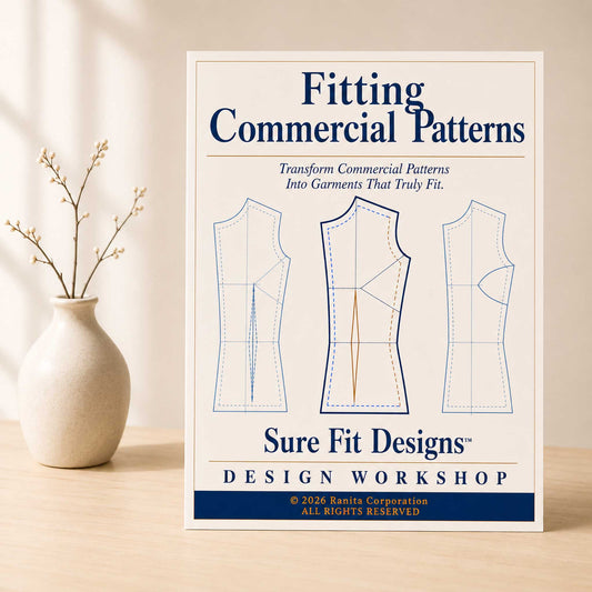 A book or booklet titled "Fitting Commercial Patterns" by Sure Fit Designs Design Workshop stands upright on a light wood surface beside a small beige vase with dried branches. The cover shows three garment pattern outlines in blue and tan on an off-white background.