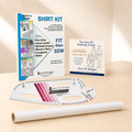 A sewing and garment-making kit displayed on a light wood surface, including a large instruction booklet, a drafting template ruler, a roll of white fabric, and a smaller course booklet. Visible branding includes Sure Fit Designs.