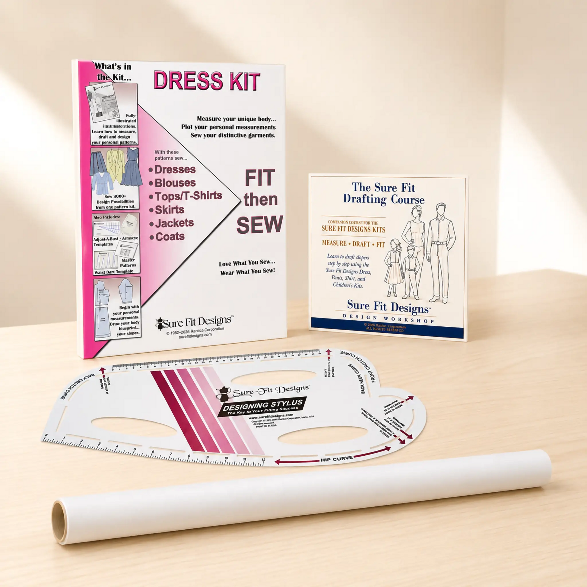 A sewing dress kit set displayed on a light wood surface, including a printed instruction booklet, a drafting course card, a curved measuring ruler, and a roll of white fabric.