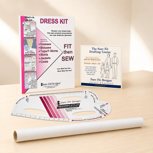 A sewing dress kit set displayed on a light wood surface, including a printed instruction booklet, a drafting course card, a curved measuring ruler, and a roll of white fabric.
