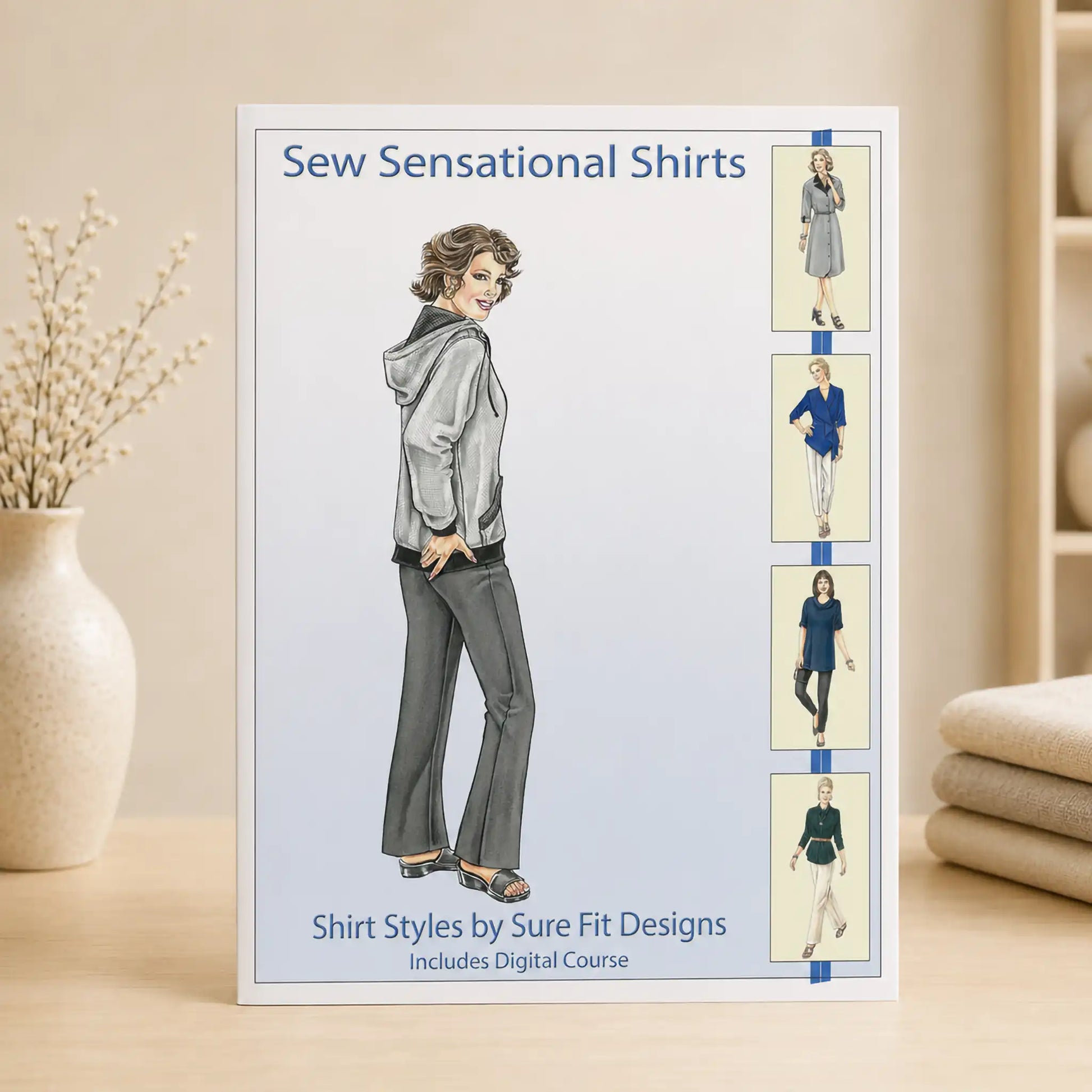A sewing pattern booklet titled 'Sew Sensational Shirts' by Sure Fit Designs stands upright on a light wood surface. The cover shows an illustrated woman wearing a gray hooded jacket and gray pants, with four smaller outfit sketches along the right side.
