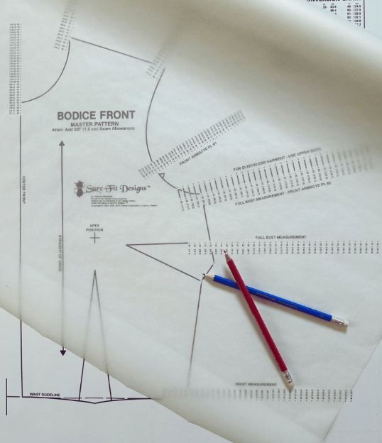 A bodice pattern sewing paper template from Sure Fit Designs, shown with two pencils (one red, one blue) on top, photographed from above.